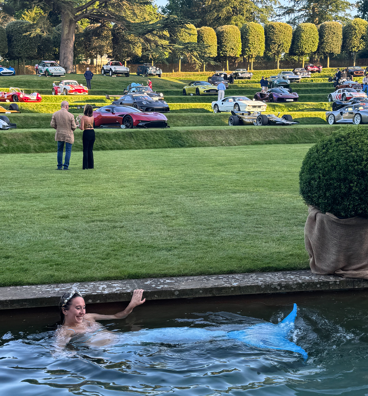 A mermaid from Aquabatix swimming in the pool in front of vintage automobiles at Heveningham Concours